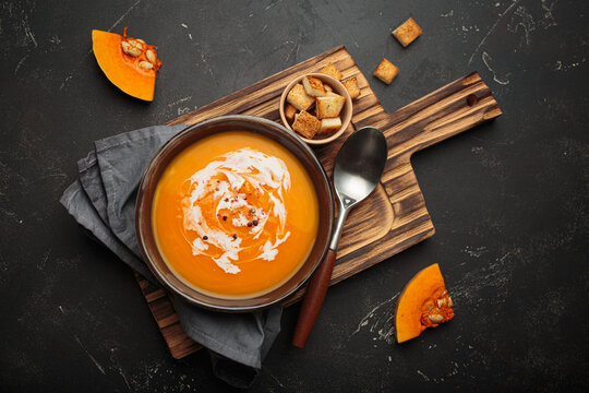 Pumpkin soup croutons cream fresh pumpkin slices wooden board dark background autumn winter