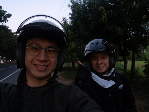 A selfie of two smiling young men wearing motorcycle helmets and jackets, motor travel concept