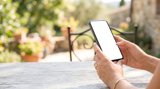 Hands holding blank screen smartphone on wooden table outdoors