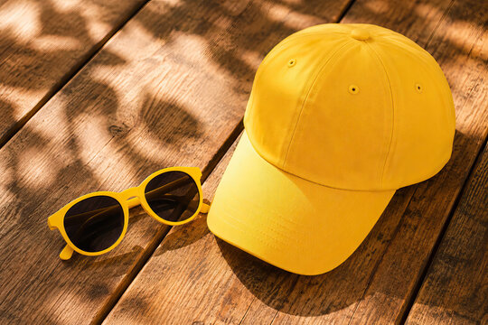 A pair of yellow sunglasses and a matching cap rest on a wooden surface, creating a stylish summer accessory image.