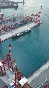Vertical aerial drone video of a modern container port with cargo ship, cranes, and shipping containers, showcasing global logistics, maritime trade, freight transportation, and supply chain.