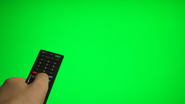 Hand holding remote control pointing at green screen TV mockup.