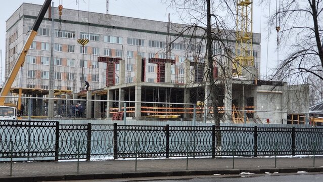 Construction of a new building in a city during winter with workers and cranes on site
