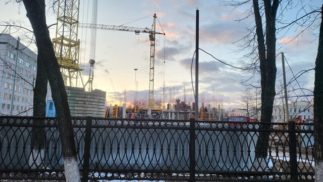 Construction site with cranes and workers during sunset in an urban area