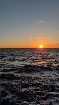 Sunset over the ocean with waves and distant island view in the evening sky