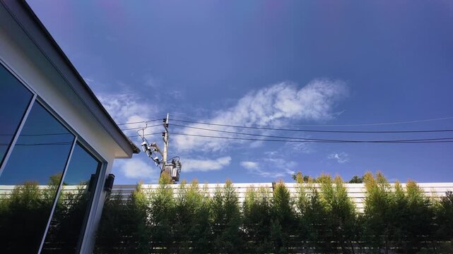Blue sky and white clouds above power lines and green bushes