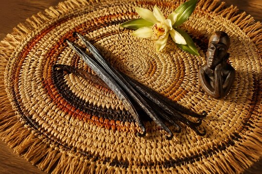 A handwoven raffia table mat with vanilla pods and a wooden carving.
