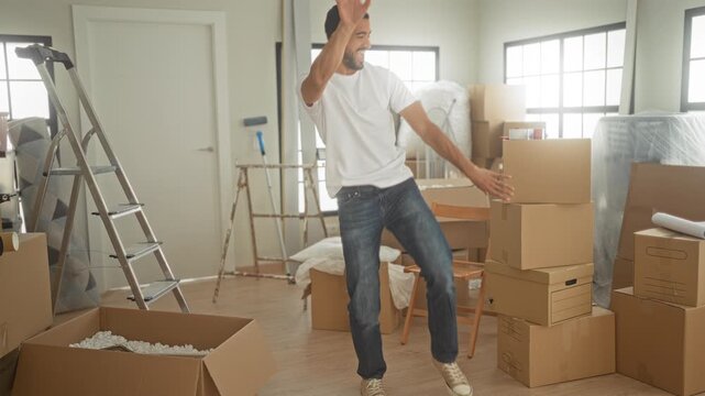Man points finger with hand at stacked cardboard boxes while dancing in a building; joy moving celebration.