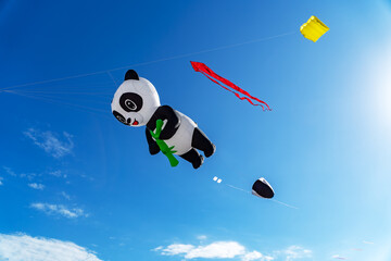 A giant inflatable panda kite holding bamboo flying high against a bright blue sky on a clear sunny day. © IgnasiusIMade