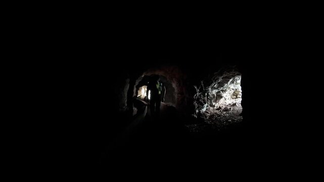 A lone hiker uses a headlamp to navigate the dark, rocky water tunnels of "Las Ventanas de G&uuml;&iacute;mar" on Tenerife, revealing the rugged interior. Emphasizes exploration and adventure.