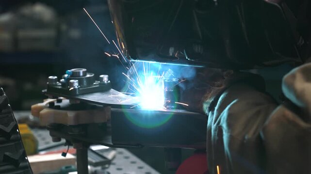 An engineer welds a frame, gear sprocket, and chassis for a homemade scooter/snowmobile with a small trailer.