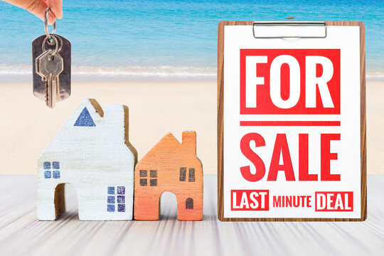Miniature house with Sale sign and house key over tropical beach background, property and real estate business concept