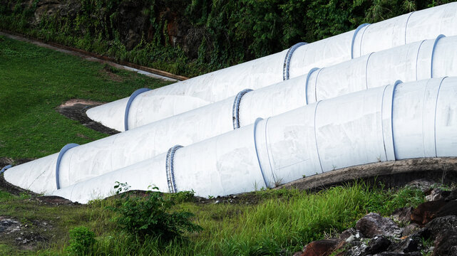 Large penstock pipelines at hydroelectric power plant with green landscape