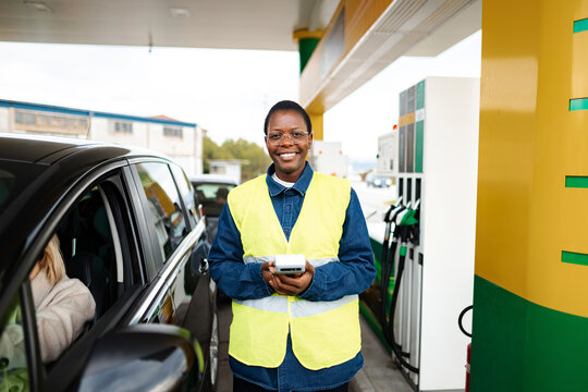 Female fuel attendant wearing a safety vest holding a payment terminal at a gas station