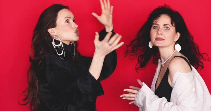 Two attractive Caucasian women having emotional discussion gesticulating with hands excited shocked facial expressions on bright red background, intense conversation dialogue stock video clip