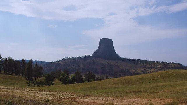 Wide View of Devils Tower across Grassy Hills and Scattered Trees