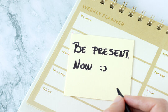 Be present, now, inspirational text note on a weekly planner. Focus, self care, and clarity concept.