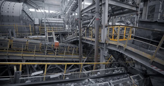 Industry Concentration factory, conveyor belts transporting ore inside metal processing plant with yellow safety railings and moving machinery.