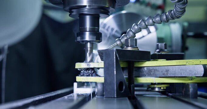 Closeup milling cutter machining metal workpiece on clamped vise inside industrial workshop under coolant flow.