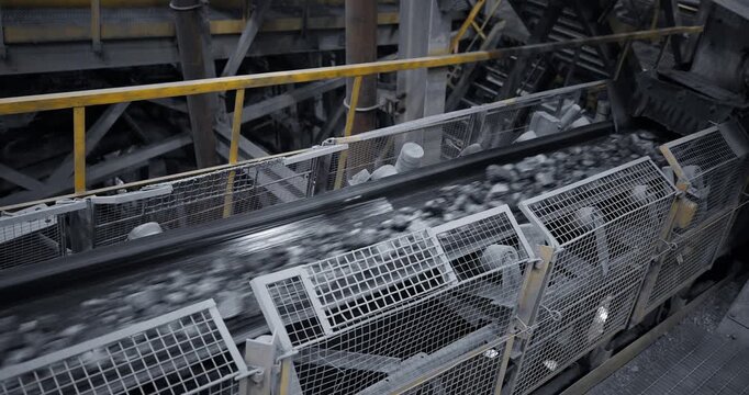 Conveyor belt transporting crushed rock and ore through industrial processing plant interior with overhead panning steady movement.