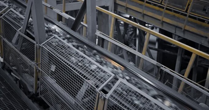Industry concentration factory, conveyor transporting crushed rock and copper ore with gold along elevated metal belt through industrial processing plant with mesh safety railings.
