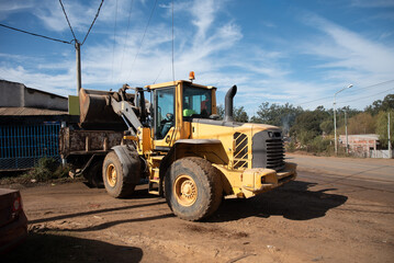 Fototapeta premium Front wheel loader lifting bucket over tipper truck at outdoor construction zone