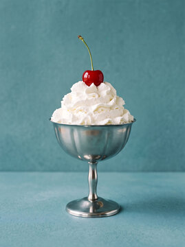 Swirled whipped cream topped with a fresh red cherry in a classic metal sundae bowl with displays single serving