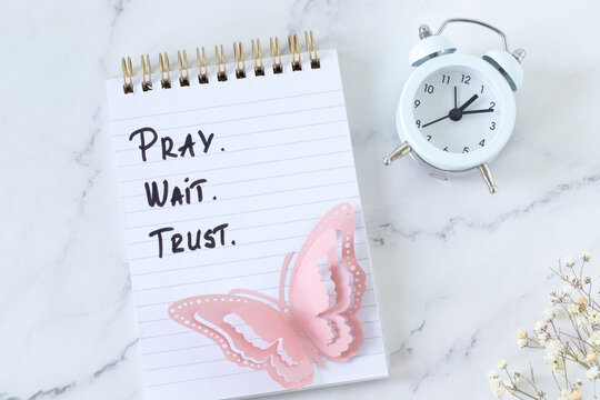 Pray, wait, trust, christian inspirational text in a notebook with alarm clock. Biblical concept of patience and faith in God Jesus Christ.