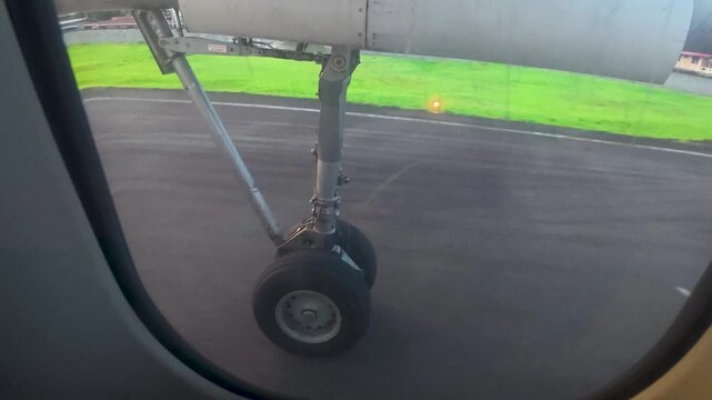 POV passenger window view of airplane landing gear retracting during takeoff over tropical coast