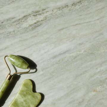 Jade face roller and gua sha on green stone background