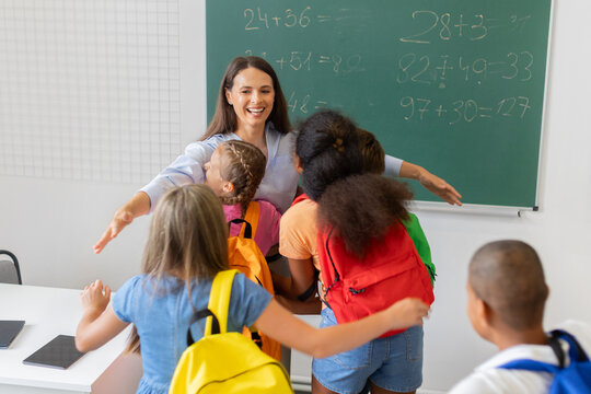 Smiling female teacher welcoming schoolchildren with colorful backpacks into warm group hug, illustrating care, trust, connection, and a supportive classroom community