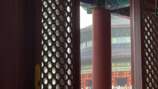 View of the Temple of Heaven through a traditional Chinese latticed window. Historic wooden building architecture with red pillar and intricate detail. Travel destination in Beijing.