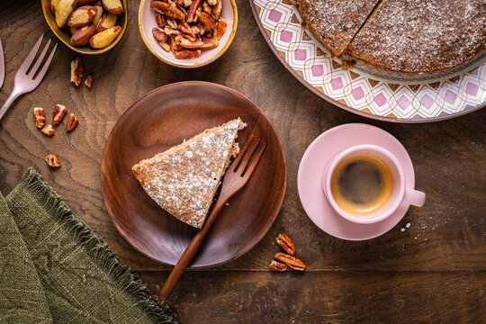 Delicious nut cake slice with espresso and scattered pecans on wooden table