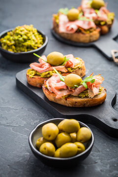 Delicious bruschetta with ham and olives served on elegant black slate