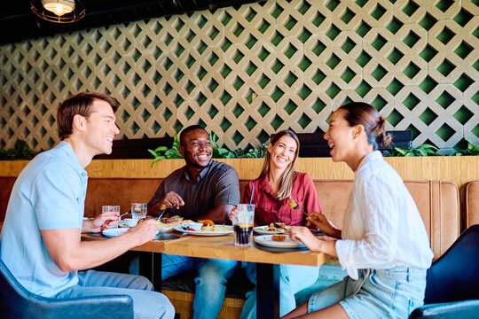 Group of diverse friends enjoying a meal and laughing while having a social gathering at a modern restaurant