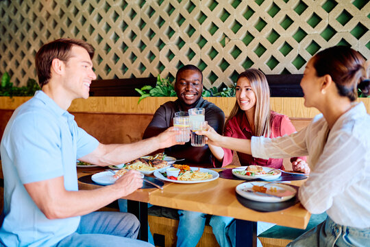 Diverse friends enjoying a celebratory meal in a restaurant, toasting with drinks and sharing happy moments