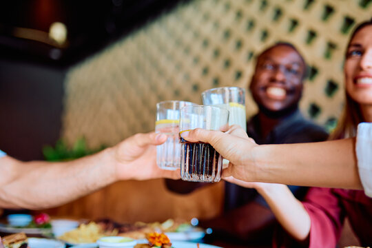 Diverse friends raising drinks, celebrating and enjoying a social gathering with food on a restaurant terrace during daytime
