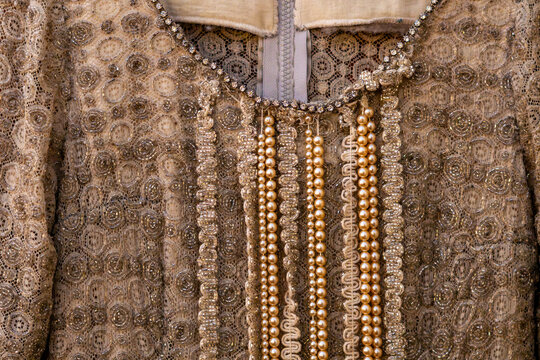 Close-up of intricate corset details on a beige lace vintage dress, embellished with hanging pearl strands, rhinestones around the neckline, and decorative trim.