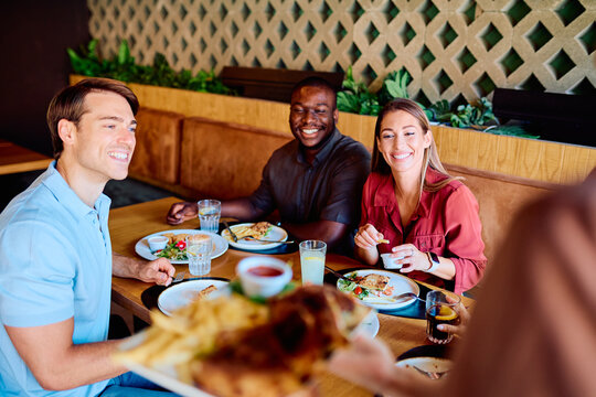 Diverse friends smiling and laughing, enjoying a meal together at a modern restaurant, sharing food and good conversation