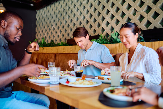 Diverse group of friends enjoying a social gathering, eating lunch and talking at a restaurant table