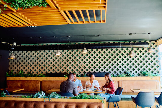 Group of four diverse people communicating and eating food at a modern restaurant, creating a social and relaxed atmosphere