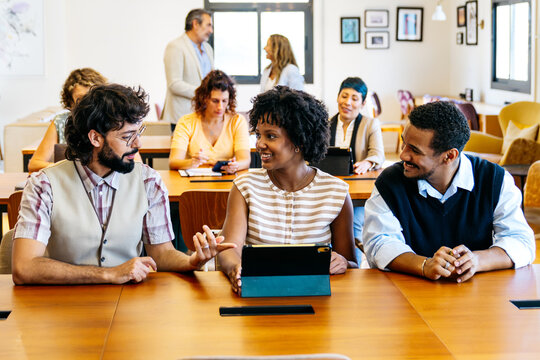 Diverse group of people working and interacting at tables in a lively, modern coworking space, fostering creativity and teamwork