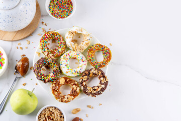 Healthy no-baked apple donuts, raw apple rounds wedges with various toppings (chocolate, vanilla fluff and peanut butter), with sugar sprinkles, chocolate chips, granola and nuts © ricka_kinamoto