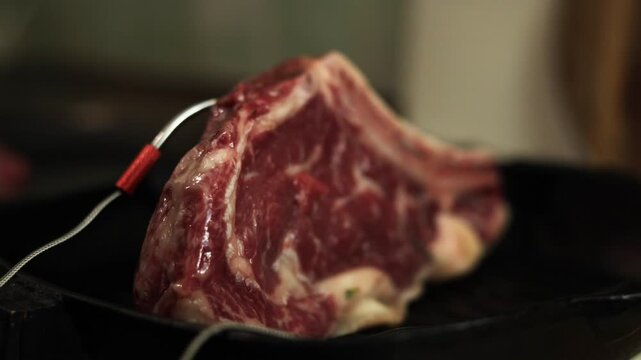 Thick cut raw beef steak with thermometer probe in cast iron pan