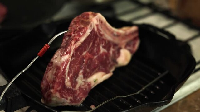 Thick bone-in steak cooking on cast iron grill pan with thermometer