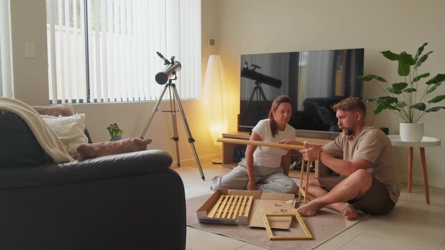 Young man and woman work together to build wooden furniture on the carpet of their bright living room