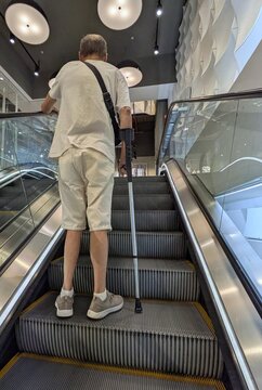 Escalera mec&aacute;nica de subida, con un hombre mayor con una muleta accediendo al primer piso de una tienda de ropa en un centro comercial