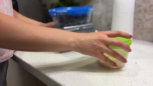 Woman preparing a healthy meal and packing plastic food containers on a kitchen counter, showcasing a daily routine for a nutritious homemade lunch to go