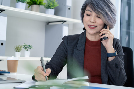 Businesswoman Taking Notes While on Phone Call in Modern Office