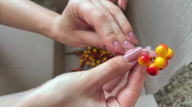 Florist's hands crafting an autumn floral arrangement with artificial berries for a festive wreath, showcasing intricate diy handiwork and creative design in a workshop
